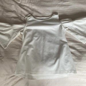 Vit topp med vida ärmar - Säljer en stilren vit topp med vida trekvartsärmar. Toppen har en offshoulder-design som ger en trendig look. Perfekt för att lyfta vilken outfit som helst.