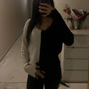 Svart och vit stickad tröja - Säljer en unik svart och vit stickad tröja med långärmad design. Tröjan har en cool asymmetrisk look med råa kanter och en croppad stil. Perfekt för att ge din outfit en edgy touch.