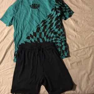 T-shirt och shorts - En turkos och svart t-shirt ihop parat med ett par marinblå shorts gjorda i funktions material, går att köpa båda separat om man skulle vilja det. Shortsen är i storlek 158/164 och tröjan är i storlek 170.