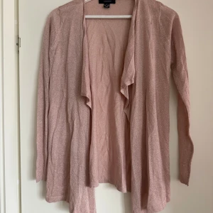 Rosa glittrig kofta från Atmosphere - Säljer en rosa glittrig kofta från Atmosphere. Den har långa ärmar och ett öppet, flödande framstycke som ger en elegant look. Perfekt för att lägga till lite glitter i vardagen. Passar bra till både jeans och klänning.