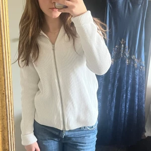 Vit ribbad kofta från Boomerang -  Säljer en stilren vit ribbad kofta från Boomerang i 100% ekologisk bomull. Koftan har en dubbel dragkedja framtill och en klassisk krage. Perfekt för en avslappnad look. Jätte bekväm och passar till många olika outfits!💕 (Lite stor på mig i bilden)