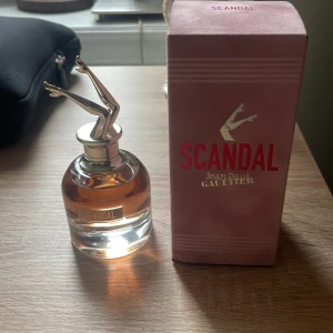 Scandal parfym från Jean Paul Gaultier - Säljer en elegant parfymflaska från Jean Paul Gaultier, Scandal. Flaskan har en unik design med en skulptural kork formad som ben i luften. Parfymen kommer i en rosa kartong med guld- och röda detaljer. Perfekt för den som vill ha en doft med attityd och stil. Endast testad.
