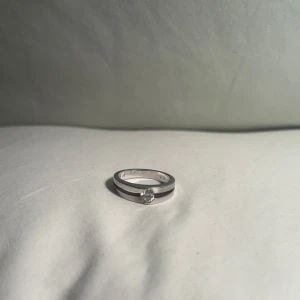 STERLING SILVERRING med klar sten/diamant - Elegant silverring med en klar sten infattad i mitten. Ringen är märkt med 925, vilket indikerar att den är gjord av sterlingsilver. Perfekt för att lägga till en subtil glans till din stil. Mycket bra skick!