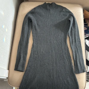 Grå ribbad klänning - Säljer en stilren grå ribbad klänning med långa ärmar och hög krage. Perfekt för kyligare dagar med sin mjuka och bekväma passform. Klänningen har en slits på sidan som ger en extra touch. Stretchig, passar både Small och Medium.