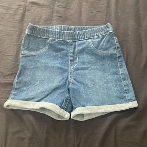 Blå jeansshorts från &Denim - Säljer ett par snygga blå jeansshorts från &Denim. De har en elastisk midja och uppvikta benslut för en avslappnad look. Perfekta för varma sommardagar!