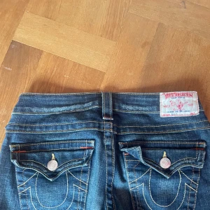 Blå jeans från True Religion w26 - Snygga blå jeans från True Religion med ikonisk broderad design på bakfickorna och slitna detaljer framtill. Säljer eftersom att dom är lite för korta❤️