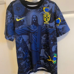 Blå fotbollströja från Nike med Brasilienmotiv - Säljer en blå fotbollströja från Nike med Brasilienmotiv och CBF-emblem. Tröjan har korta ärmar och ett unikt mönster med gula detaljer. Perfekt för fotbollsfans som vill sticka ut på planen!