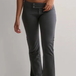 Grå lågmidjade byxor - Snygga grå lågmidjade byxor med bootcut-stil och två knappar framtill. Endast provade, storlek S. 