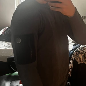 Grå tröja från Snoot - Näst intill ny tröja från Snoot i storlek XXL som tyvärr har krympt i tvätten(sitter som M nu). Tröjan har en praktisk ficka med dragkedja på ärmen och en rund halsringning. Perfekt för en stilren och bekväm look.