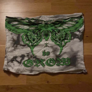 Grön och svart tubtop med fjärilsmotiv - Snygg tubtop med ett stort grönt fjärilsmotiv och text i gotisk stil. Toppen har en batikmönstrad bas i svart och vit. Knappt använd förutom när jag först provade den.