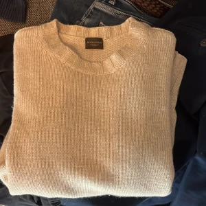 Rose & Born tröja - Säljer en stilren beige stickad tröja från Rose & Born. Tröjan har en klassisk rund hals och ribbade muddar vid ärmslut och nederkant. Perfekt för kyligare dagar. 100% Kashmir 6,500kr ny pris 