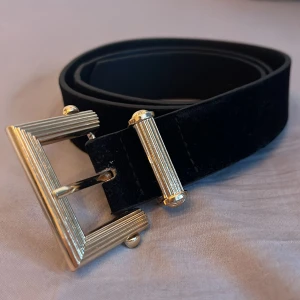 Svart bälte med guldfärgat spänne - Snyggt svart bälte med ett stilrent guldfärgat spänne. Bältet har en slät yta och flera justerbara hål för perfekt passform. Perfekt för att ge en elegant touch till din outfit.