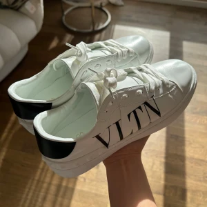 Vita sneakers från Valentino  - Snygga vita sneakers från Valentino med svart VLTN-logga på sidan. Skorna har snörning och en stilren design med svarta detaljer på hälen. Perfekta för en trendig look.🫶🏼(men har inte någon låda till skorna)