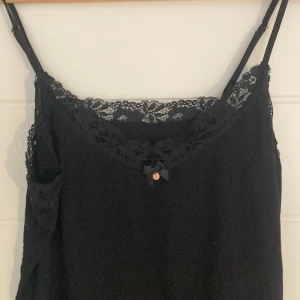 Svart linne med spetsdetaljer - Säljer ett svart linne med spetskant vid halsringningen och nederkanten. Linnet har små detaljer i lite rosa/guld färg💗tryck gärna på köp nu, pris kan diskuteras💗💗