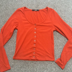 Röd ribbad topp från Bik Bok - Säljer en snygg röd ribbad topp från Bik Bok i storlek XS, (funkar även lika bra som S!!) Toppen har långa ärmar och knappar framtill, vilket ger den en stilren look. Perfekt för både vardag och fest! Perfekt färg nu till hösten! 