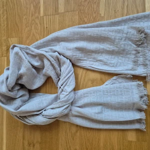 Halsduk Tommy Hilfiger - Halsduk från märket TommyHilfiger. Ljus beige färg. Väldigt mjuk och len material. Små fransar på vardera sida. 180 cm lång och 56 cm bred. Använd fåtal gånger. Bomull och viskos material. 