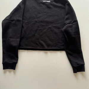 Svart croppad tröja från NA-KD - Säljer en svart croppad tröja från NA-KD. Den är supermjuk och perfekt för en casual look. Tröjan har långa ärmar och en ribbad krage. Passar perfekt till både jeans och kjol för en avslappnad stil. Perfekt för höst och vår!