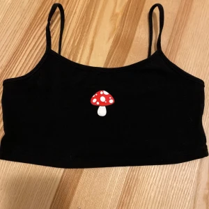 Svart linnetopp  - Säljer en svart croppad linnetopp med smala axelband och ett sött rött svampmotiv på framsidan. Strl 140, 10 year. 