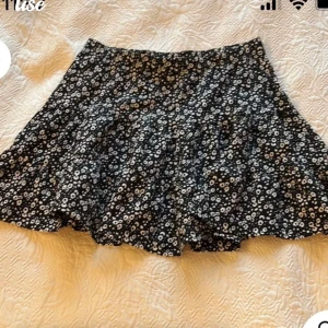 Svart blommig kortkjol - Charmig svart kortkjol med ett sött blommönster i vitt. Perfekt för en avslappnad och stilfull look. Kjolen har en luftig passform som ger en skön känsla.