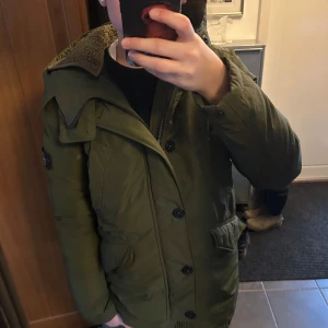 Grön vinterjacka från Stone Island - Säljer en grön dunjacka från Stone Island med en mysig fodrad insida. Jackan har en huva och stängs med både dragkedja och knappar. Perfekt för kyliga dagar med sin stilrena design och praktiska fickor. Skulle säga den passar någon mellan 170-175 perfekt 👌 👊