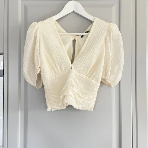 Vit blus från Gina Tricot - Säljer en söt vit blus från Gina Tricot med puffiga ärmar och knytning i ryggen. Blusen har en v-ringad design och är tillverkad i ett lätt och luftigt material, den är supersöt och använd vid ett skolavslutningatillfälle🤍 Bild tre är bäst för att se hur färgen ser ut.