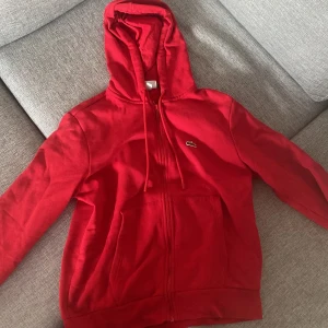 Lacoste Hoodie Röd - Lacoste hoodie Röd med storlek M är i mycket bra skick, endast använd ett fåtal gånger. Ordinarie pris på hoodien var 1200 kr och nu säljs den på 899 kr i ett mycket bra skick