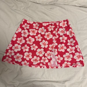 Röd blommig strand kortkjol - Säljer en superfin röd strand kortkjol med stora vita blommor. Kjolen har en omlott-design och är gjord av ett stretchigt material som känns bekvämt. Perfekt för sommarens varma dagar! 🌸