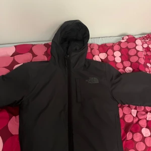 Svart jacka från The North Face - Säljer en svart jacka från The North Face med huva och dragkedja. Perfekt för kyligare dagar med sin stilrena design och funktionella detaljer.