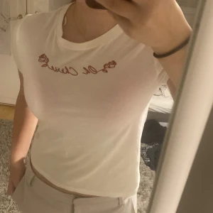 Vit t-shirt från H&M Divided - Säljer en vit t-shirt från H&M Divided med texten 'Oh Chérie' och rosdetaljer i rött på bröstet. T-shirten är kortärmad och har en klassisk rund halsringning. Perfekt för en avslappnad stil.