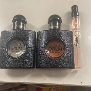 Yves Saint Laurent Black Opium Parfym - Säljer två flaskor av Yves Saint Laurent Black Opium parfym. Flaskorna har en glittrig svart design med runda fönster som visar parfymens färg. En av flaskorna har en ljusare nyans medan den andra är mörkare. Inkluderar även en smidig resestorlek i en genomskinlig flaska med svart lock. 850 för alla 3 Box medföljer 
