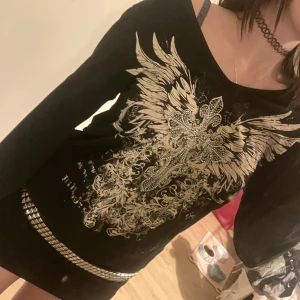 Svart tröja med luva och mönster  - Snygg svart tröjhoodie med ett stort, detaljerat vingmönster på framsidan. Jag har på outfiten en svart kjol till, tröjan går ungefär ner till bältet