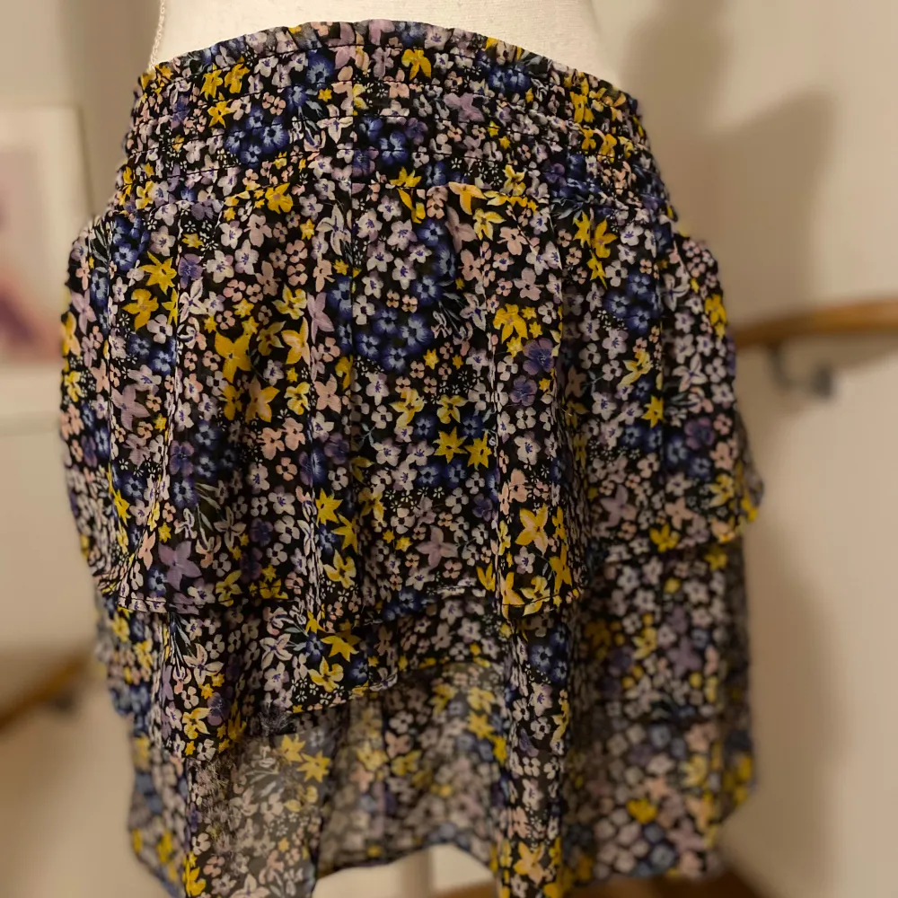 Säljer en söt blommig kjol från H&M med ett färgglatt mönster i rosa, gult och lila. Kjolen har en luftig design med volanger som ger en fin rörelse. Lite sliten på 2 ställen u volang 3 men syns knappt. Perfekt för att liva upp garderoben!. Hameet.