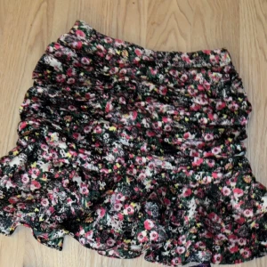 Blommiga kjolar med volang - Två färgglada blommiga kjolar med volangdetaljer. Den ena har en bas i svart med rosa och vita blommor, medan den andra har en mörk marinblå färg med lila och orange blommor. Älskar dessa kjolar men kan tyvärr inte ha dem längre på grund av graviditet. Super snygga med boots✨😍båda säljs för 45 men pris kan diskuteras vid snabb affär