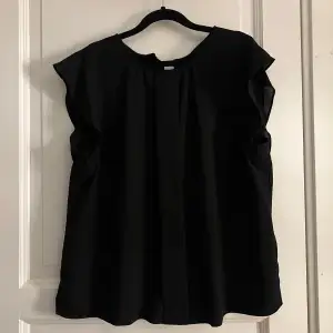 Elegant svart blus med korta ärmar och knappar längs ryggen. Perfekt för en stilren look.