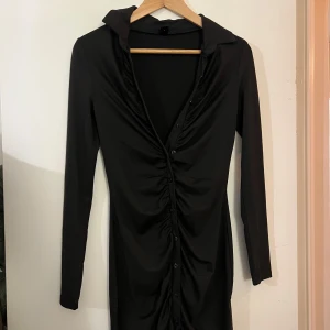 Svart klänning från Shein - Snygg svart klänning från Shein med långa ärmar och knappar framtill. Klänningen har en åtsittande passform och en stilren design som passar perfekt för olika tillfällen. Tillverkad i ett mjukt och bekvämt material.