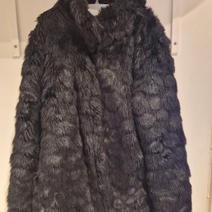 Svart pälsjacka från Name It - Säljer en snygg svart pälsjacka från Name It. Jackan har en mjuk och fluffig yta med långa ärmar och knäppning framtill och två fickor.