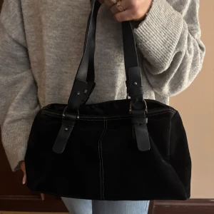 Svart axelväska i mocka - Snygg svart axelväska i mjuk mocka med stilrena detaljer. Väskan har två rejäla handtag och en praktisk dragkedja upptill. Perfekt för att bära med sig det viktigaste med stil.