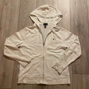 Vit hoodie från Ralph Lauren - Säljer en stilren vit hoodie från Ralph Lauren med dragkedja och det klassiska broderade logotypen på bröstet. Perfekt för en avslappnad look. Hoodien har långa ärmar och en bekväm passform. Använd endast ett par gånger 🤩priset är ej hugget i 🪨storlek 170. Skick 9,5/10 orginalpris 1200 mitt pris är endast 400🤩