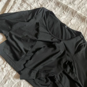 Svart croppad topp - Säljer en svart croppad topp med rund halsringning. Toppen har en enkel design och är perfekt för en stilren look. Passar bra till både jeans och kjol.
