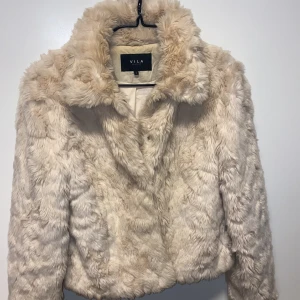 Beige pälsjacka från VILA - Säljer en supermjuk och fluffig beige pälsjacka ( ej äkta päls ) från VILA. Jackan har en klassisk krage och är perfekt för att hålla dig varm och stilren under kyliga dagar. Den är långärmad och har en snygg, lyxig look. Perfekt för att lyfta vilken outfit som helst!