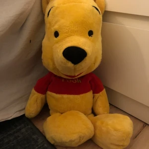 Stor nallebjörn i gult och rött - Säljer en stor och mjuk nallebjörn i gult med en röd tröja. Perfekt för kramar och som dekoration i barnrummet. Den har svarta detaljer på nos och ögon.