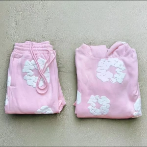 Denim tear tracksuit  - Säljer en söt rosa hoodie och byxa med vita blommiga detaljer. Tröjan har en klassisk huva och en stor ficka framtill. Perfekt för en avslappnad stil.