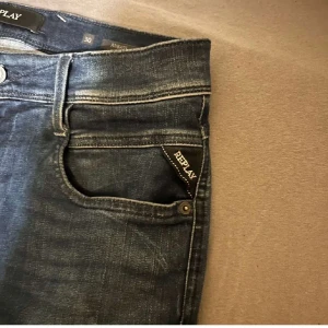 Mörkblå jeans från Replay - Snygga mörkblå jeans från Replay med klassisk femficksdesign och knappgylf. Perfekta för en stilren look. Märkeslogga på fickan ger en extra touch.