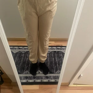 Beige byxor - Snygga beige byxor med elastisk midja och avslappnad passform. Perfekta för en bekväm och stilren look. Byxorna har fickor på sidorna och är tillverkade i ett mjukt material.