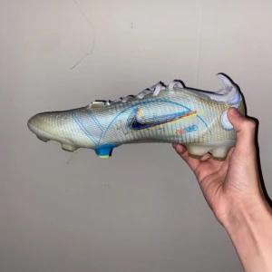 Nike fotbollsskor med färgglada detaljer - Snygga fotbollsskor från Nike med en unik design i vitt och blått. Skorna har färgglada detaljer och snörning för perfekt passform. Perfekta för fotbollsplanen! Priset kan diskuteras!!