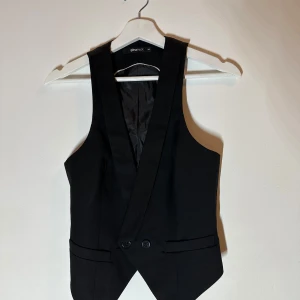 Svart väst från Gina Tricot - Snygg svart väst från Gina Tricot med knappar framtill. Perfekt för att ge en stilren touch till din outfit. Västen har en klassisk design med en elegant passform.🥰🥰🥰