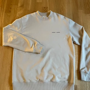 Beige sweatshirt från Samsøe Samsøe - Säljer en stilren beige sweatshirt från Samsøe Samsøe. Tröjan har långa ärmar och en rund halsringning med ribbade muddar vid ärmslut och nederkant. Perfekt för en avslappnad look.