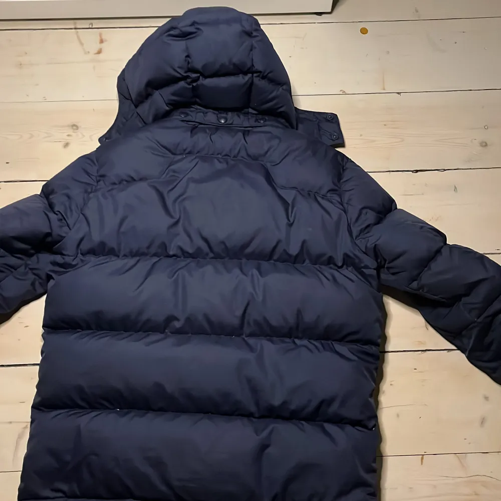 Säljer en snygg mörkblå puffer jacket från Ralph Lauren. Jackan har en dragkedja framtill och en broderad logotyp på bröstet. Perfekt för kalla dagar med sin vadderade design och huva.. Takit.