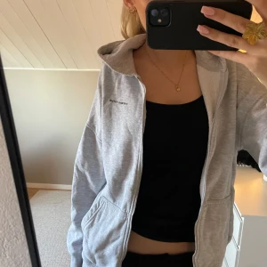 Grå huvtröja från Notion of Form - Säljer en stilren grå huvtröja. Tröjan har dragkedja och en bekväm huva. Perfekt för en avslappnad look. Passar till det mesta och är ett måste i garderoben!