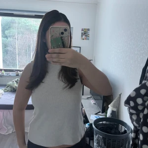 Vit ärmlös polotopp - Säljer en stilren vit/beige ärmlös polotopp. Perfekt för lager-på-lager eller att bära som den är. Toppens ribbade material ger en snygg och bekväm passform.